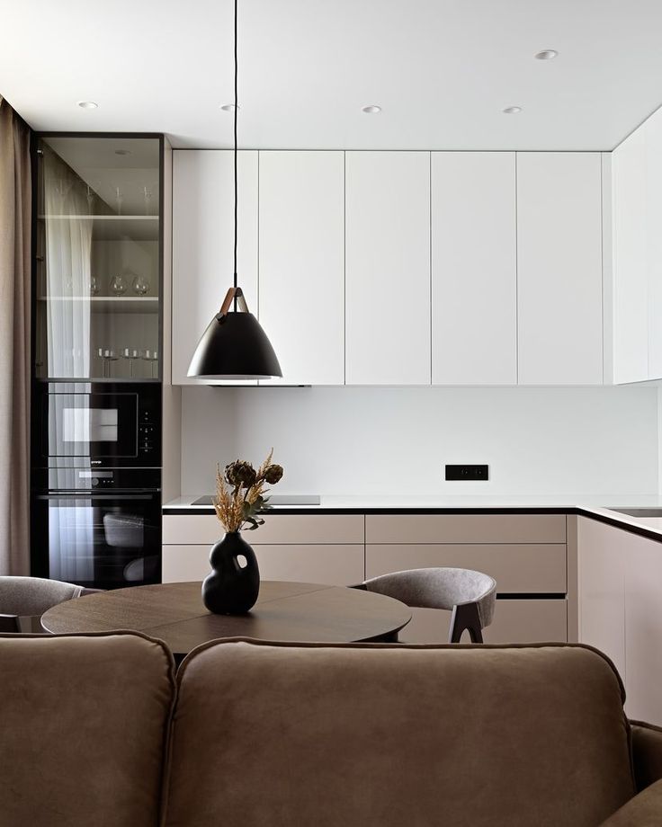 a living room and kitchen area with couches, table, cabinets and lights hanging from the ceiling