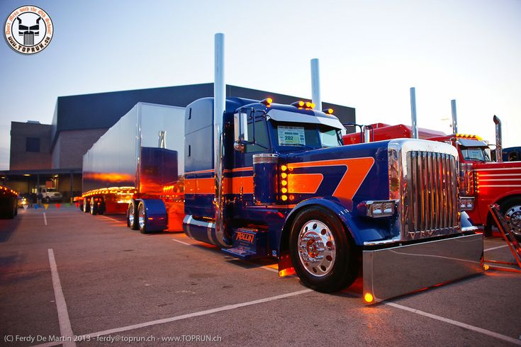 several semi trucks parked in a parking lot at dusk with the sun setting behind them