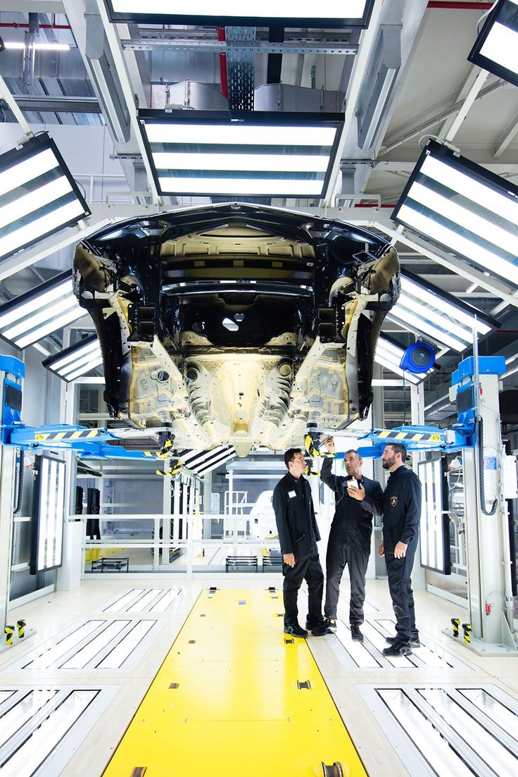 two men standing in front of an assembly line looking at something on the floor that is being worked on