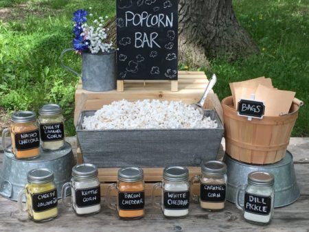 an outdoor popcorn bar with chalkboard signs and buckets full of popcorn sits on a picnic table