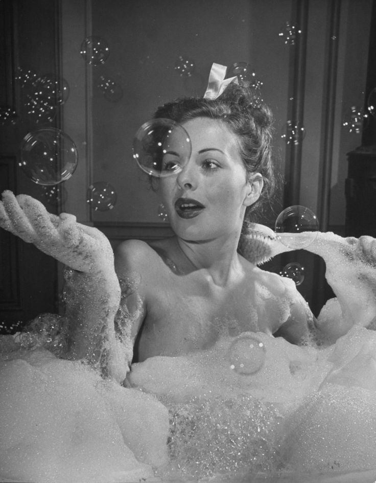 a woman sitting in a bubble filled bathtub with soap bubbles floating over her face