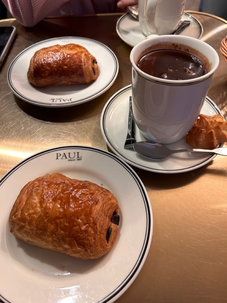 two croissants and a cup of coffee sit on the table in front of each other