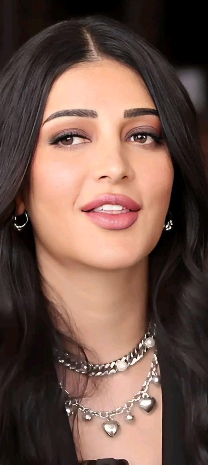 a woman with long black hair wearing a choker and earrings on her neck is smiling at the camera