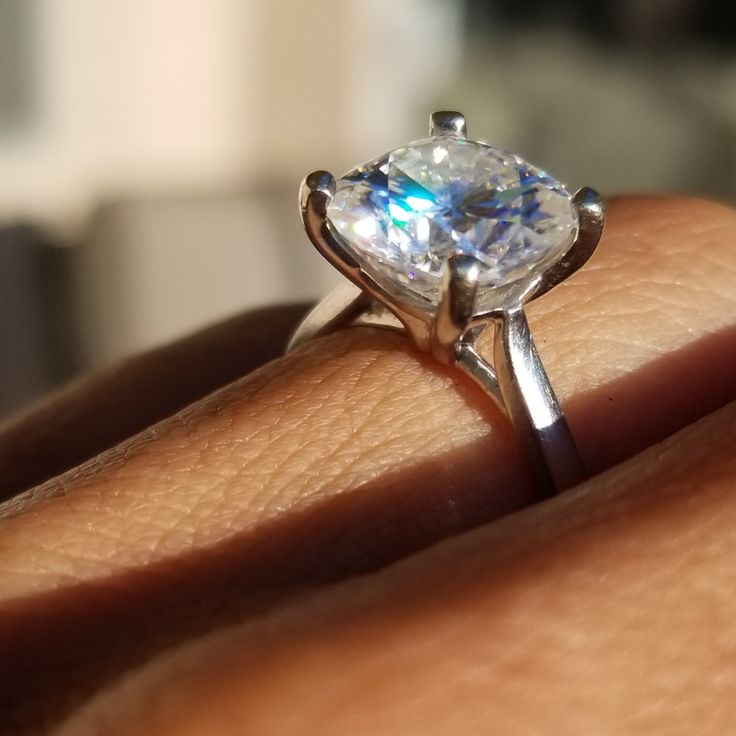 a woman's hand holding a ring with a large diamond in the center, on top of her finger