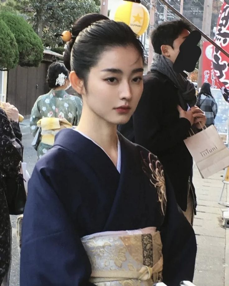 a woman dressed in traditional japanese clothing on the street with other people walking around her