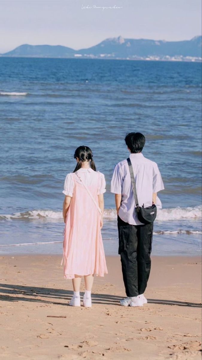 two people standing on the beach looking out at the water