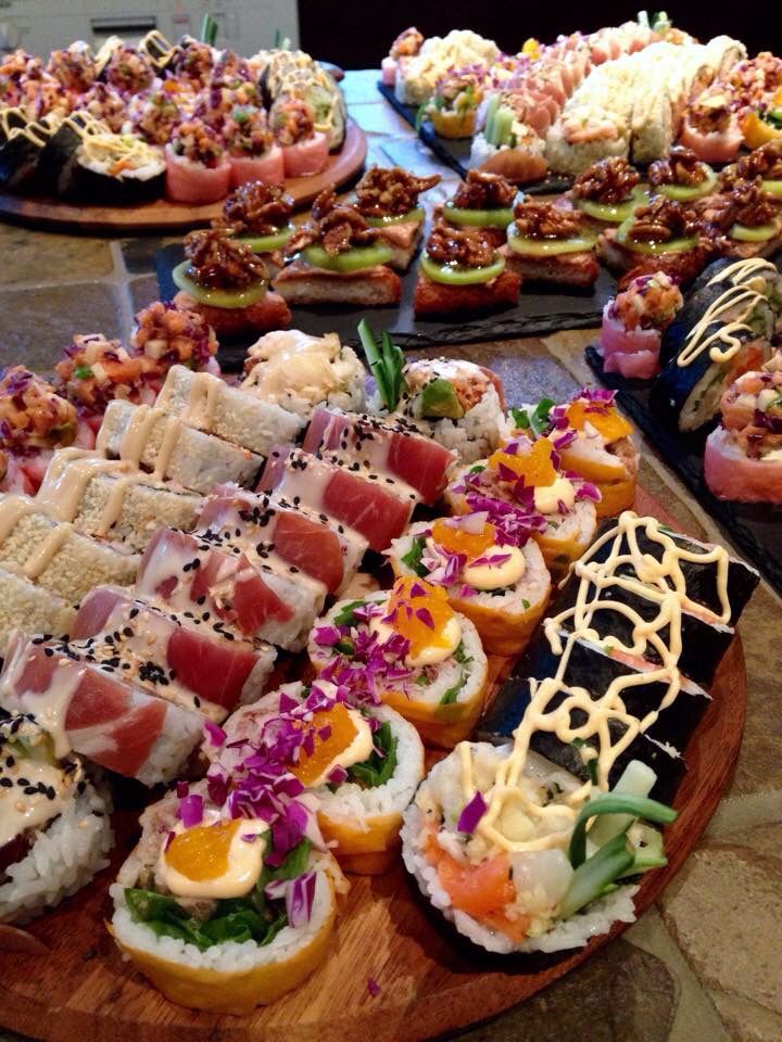 many different types of sushi are displayed on a wooden platter, along with other appetizers