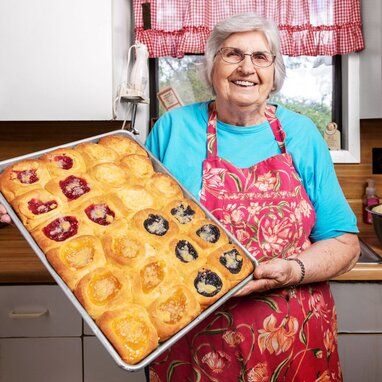 an older woman holding a pan full of baked goods