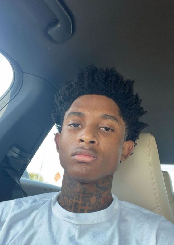 a man with tattoos on his neck sitting in the back seat of a car looking at the camera