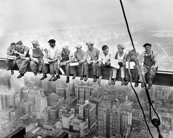 a group of men sitting on top of a tall building next to each other in front of a city