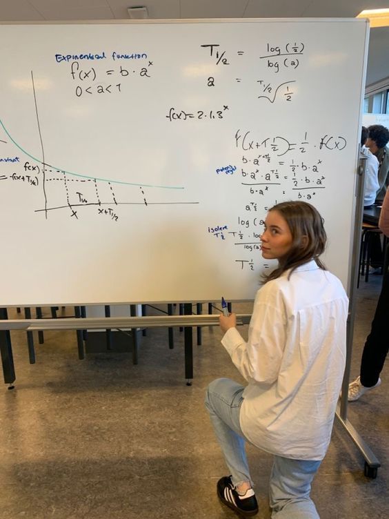 a woman standing in front of a whiteboard with writing on it and another person behind her