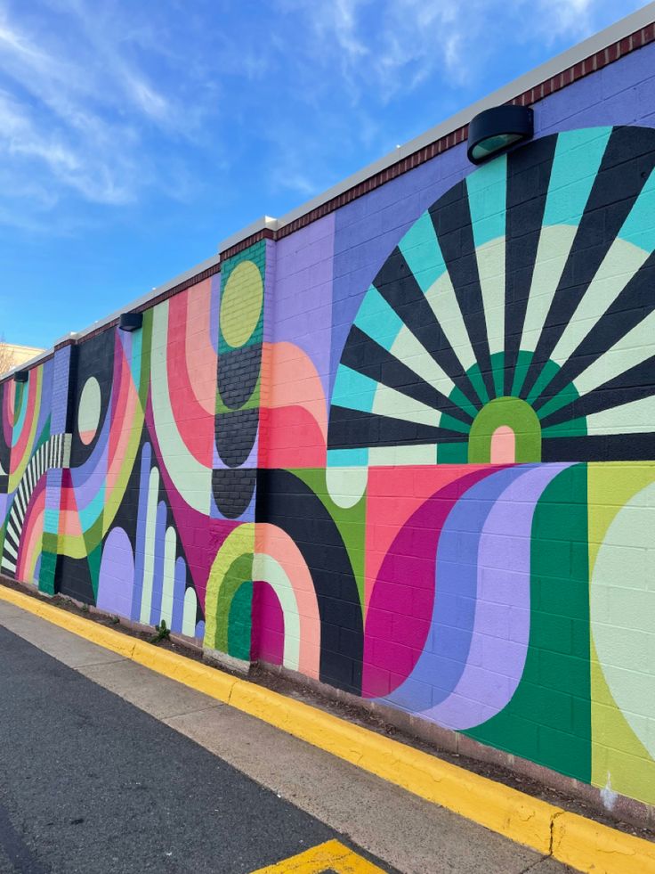 a colorful mural on the side of a building in front of a blue sky with white clouds