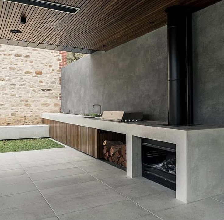 an outdoor fireplace in the middle of a patio with a stone wall and wooden ceiling