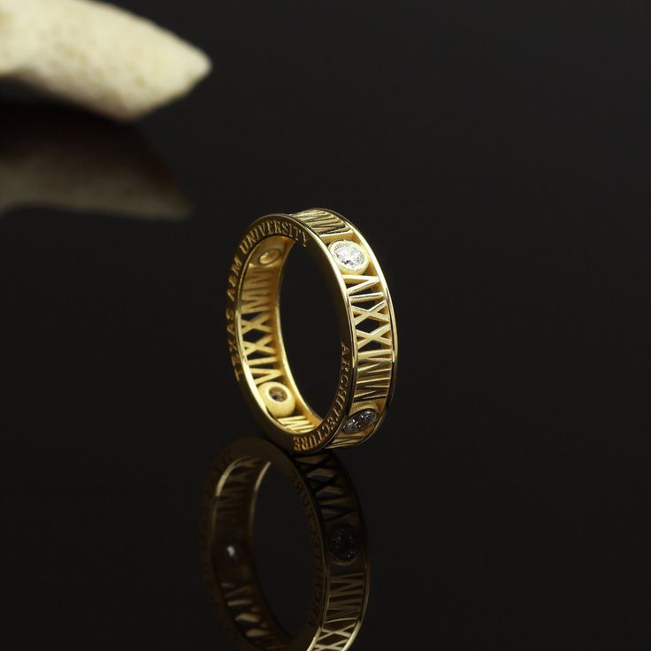 a gold wedding ring with roman numerals on the side and diamonds in the middle