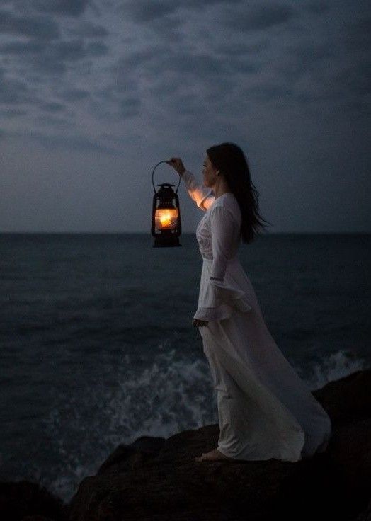 a woman is holding a lantern by the ocean