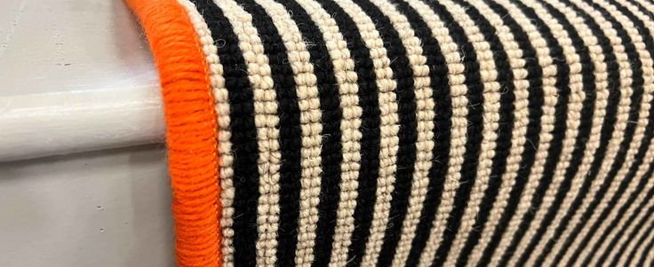 an orange and black striped rug hanging on a white wall next to a metal hook