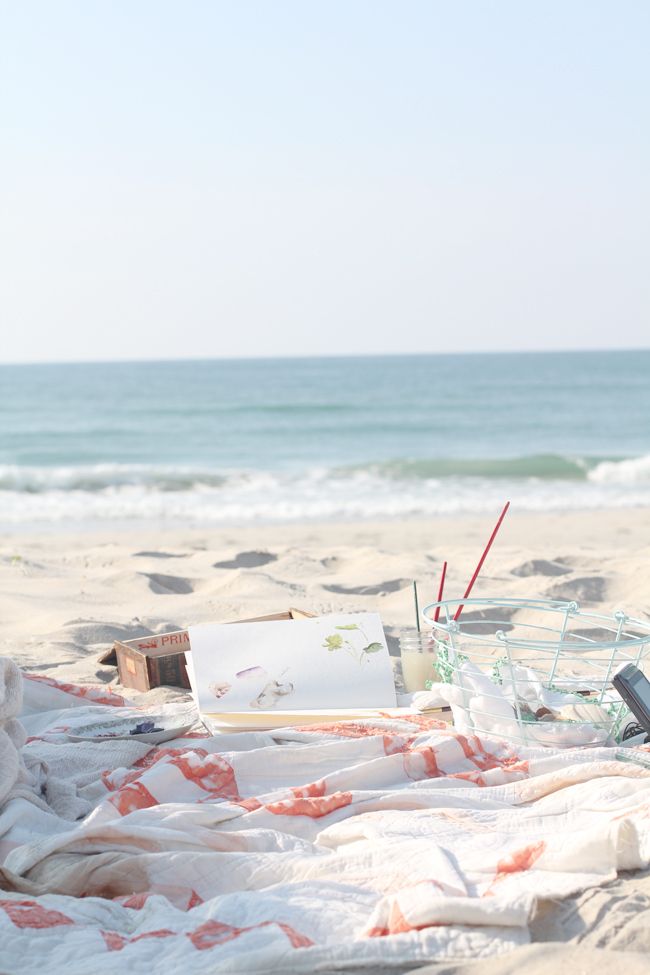 an open laptop computer sitting on top of a beach covered in blankets next to the ocean