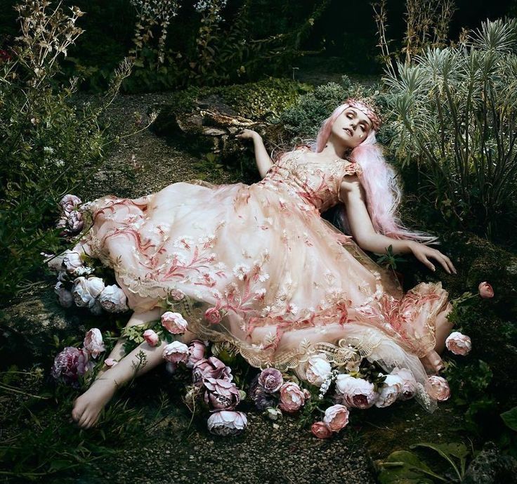 a woman is laying on the ground surrounded by flowers and plants, with her hair blowing in the wind