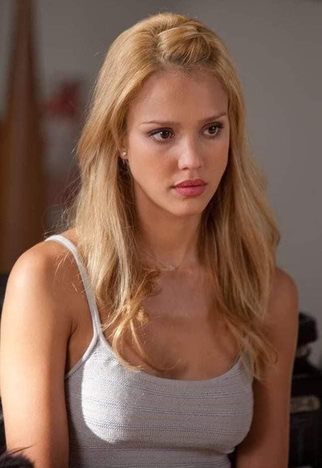 a woman with long blonde hair sitting in front of a table and looking at the camera