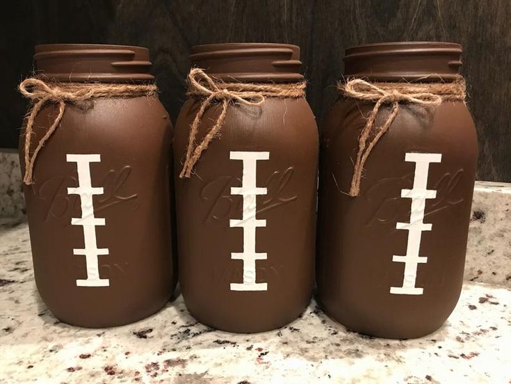 three brown mason jars with white footballs painted on them