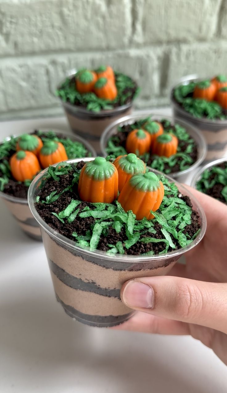 a hand holding a cup filled with green frosting and small pumpkins on top