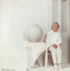 an old man sitting on a chair next to a vase