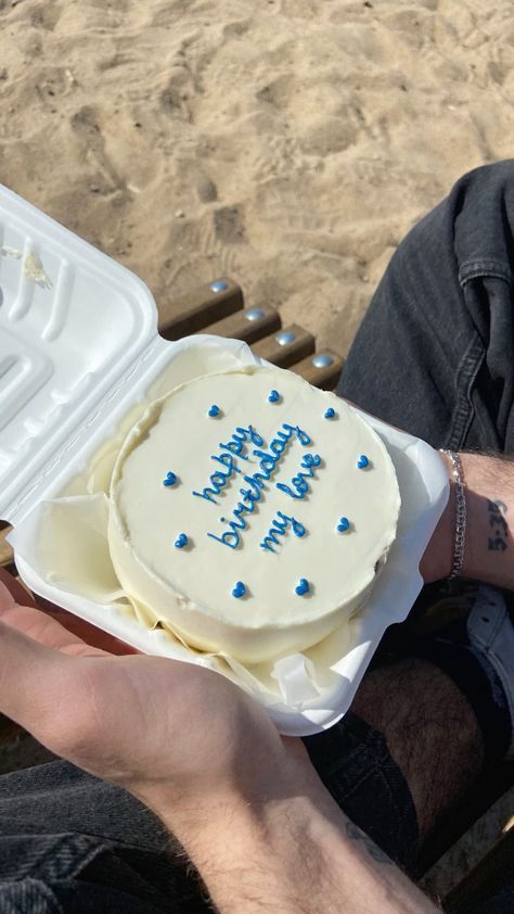 a man is holding a cake with blue frosting on it in front of the beach