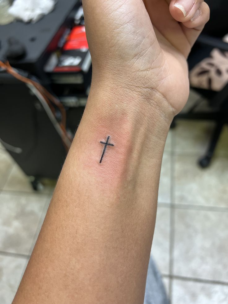 a person with a small cross tattoo on their wrist