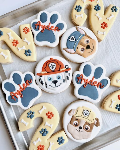 decorated cookies in the shape of paw prints on a cookie sheet with dog's names