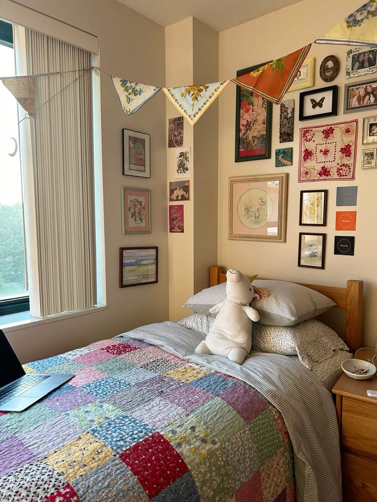 a bed with a quilt and stuffed animal sitting on top of it next to a window