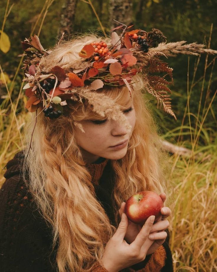 a woman with long blonde hair holding an apple in her hands and wearing a wreath on her head