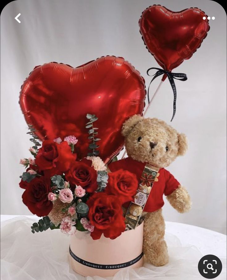 a teddy bear sitting on top of a vase filled with red roses and heart shaped balloons