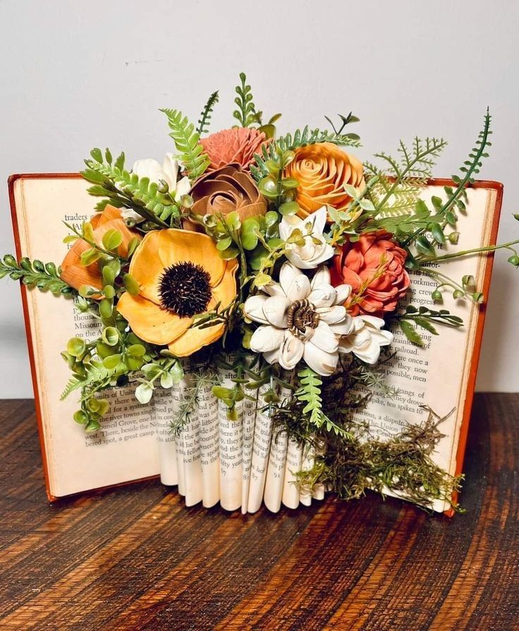 an open book with flowers and greenery on it