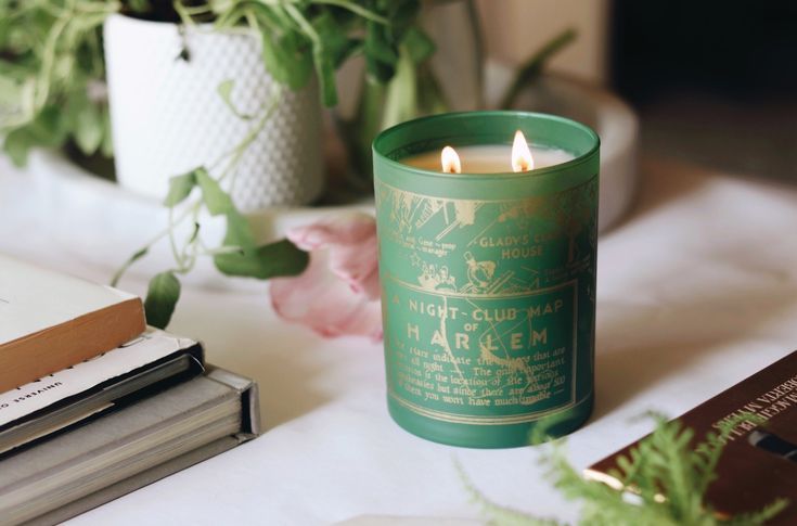 a green candle sitting on top of a table next to some books and flowers in vases