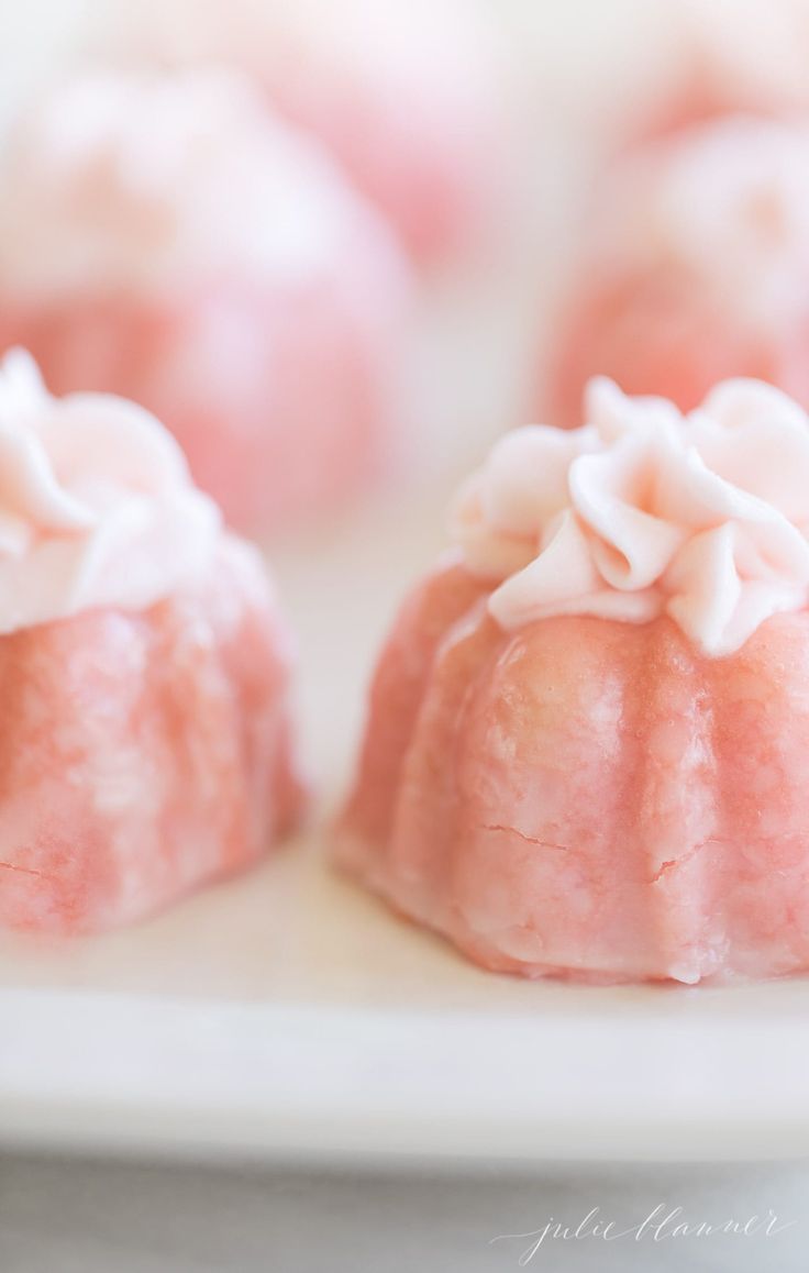 small pink desserts on a white plate with frosting and sprinkles