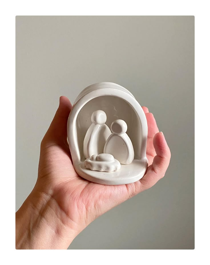 a hand holding a white ceramic figurine with a baby in it's lap