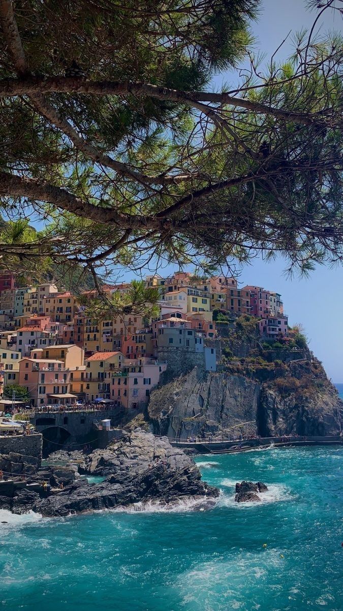 the village is perched on top of a cliff by the ocean with waves crashing in front of it