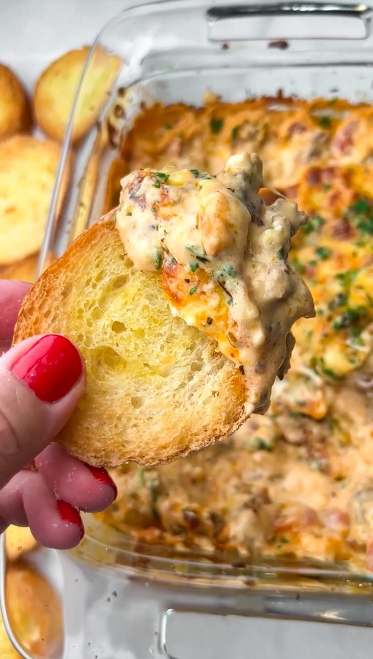 a hand holding up a piece of bread that has been dipped with cheese and sauce