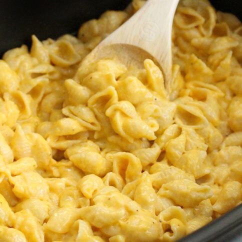 macaroni and cheese being stirred with a wooden spoon in a slow cooker