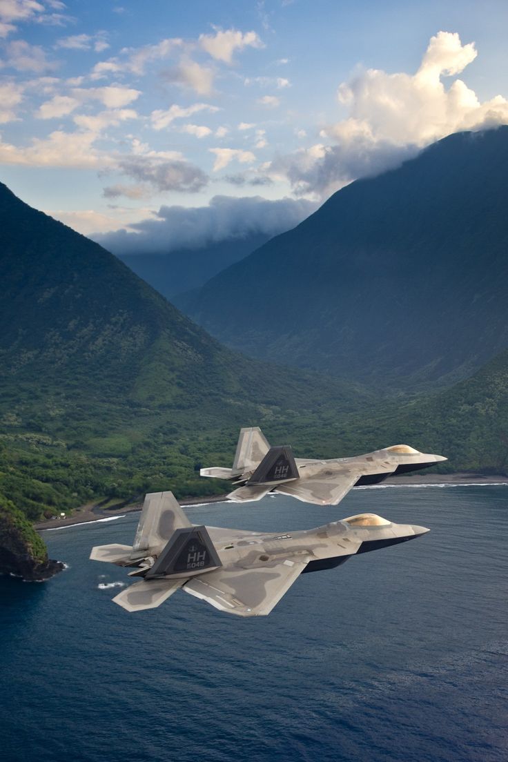 two fighter jets flying over the ocean near mountains