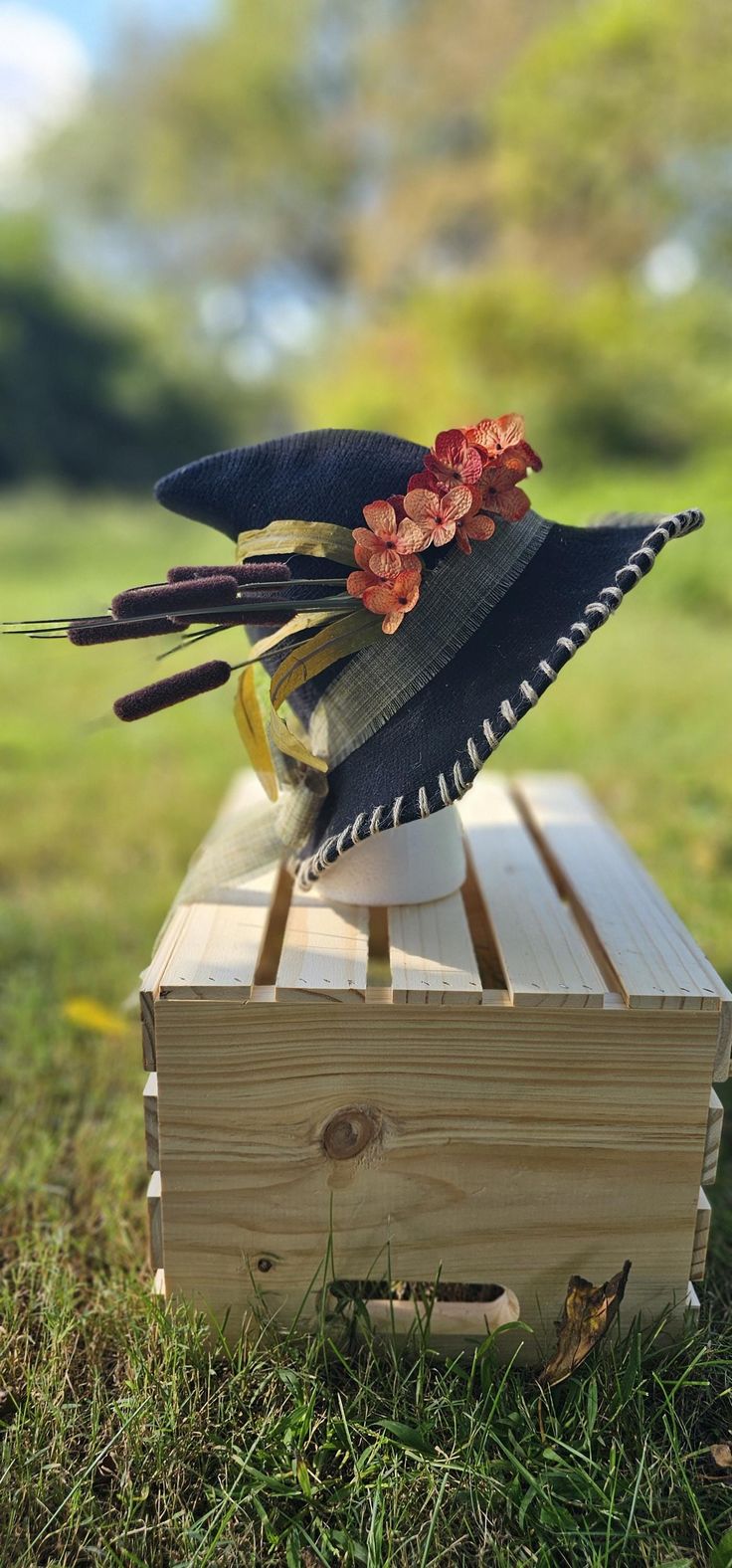 a hat with flowers is sitting on top of a wooden box in the middle of some grass