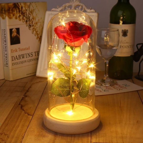 a red rose in a glass dome with fairy lights on the base and wine bottle behind it