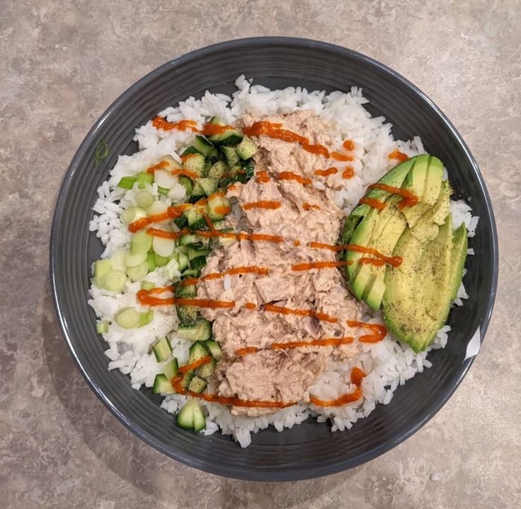 a plate filled with rice, cucumber and meat on top of it next to an avocado