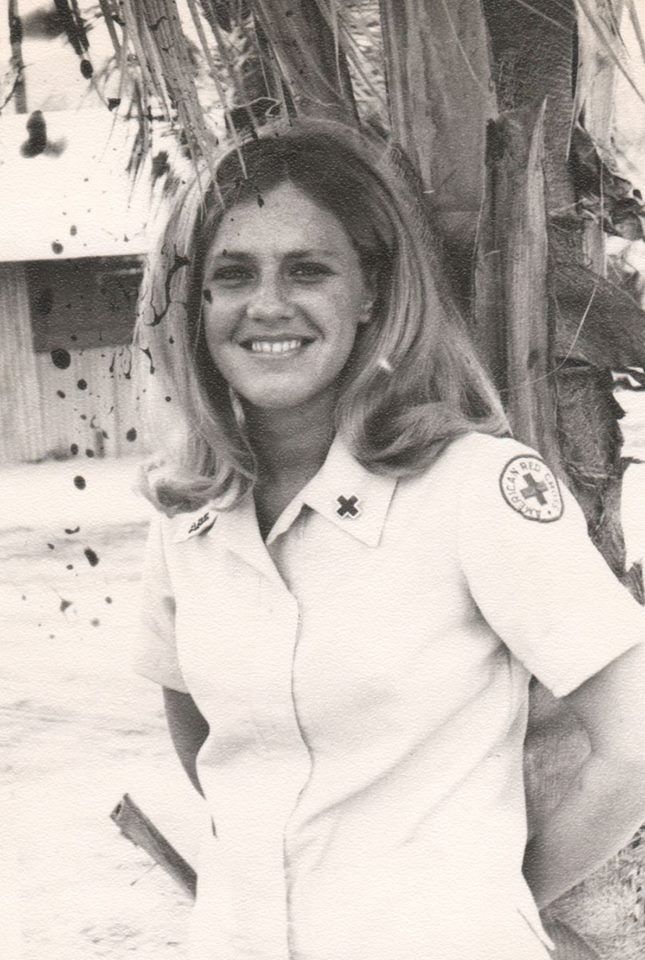 a woman in uniform standing next to a palm tree and smiling at the camera with her hands on her hips