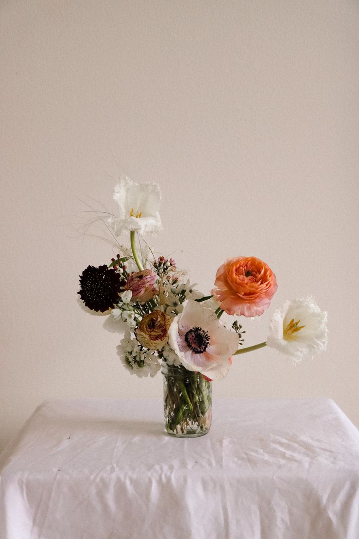 an arrangement of flowers in a glass vase on a white tablecloth with a plain background