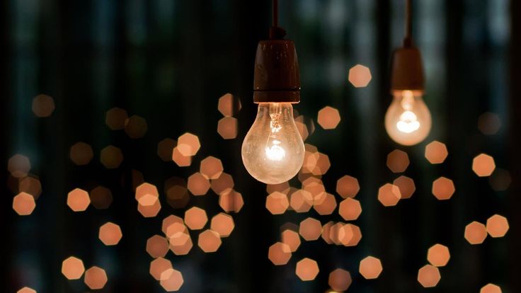 several light bulbs hanging from strings with lights in the background and blurry lights on the wall behind them