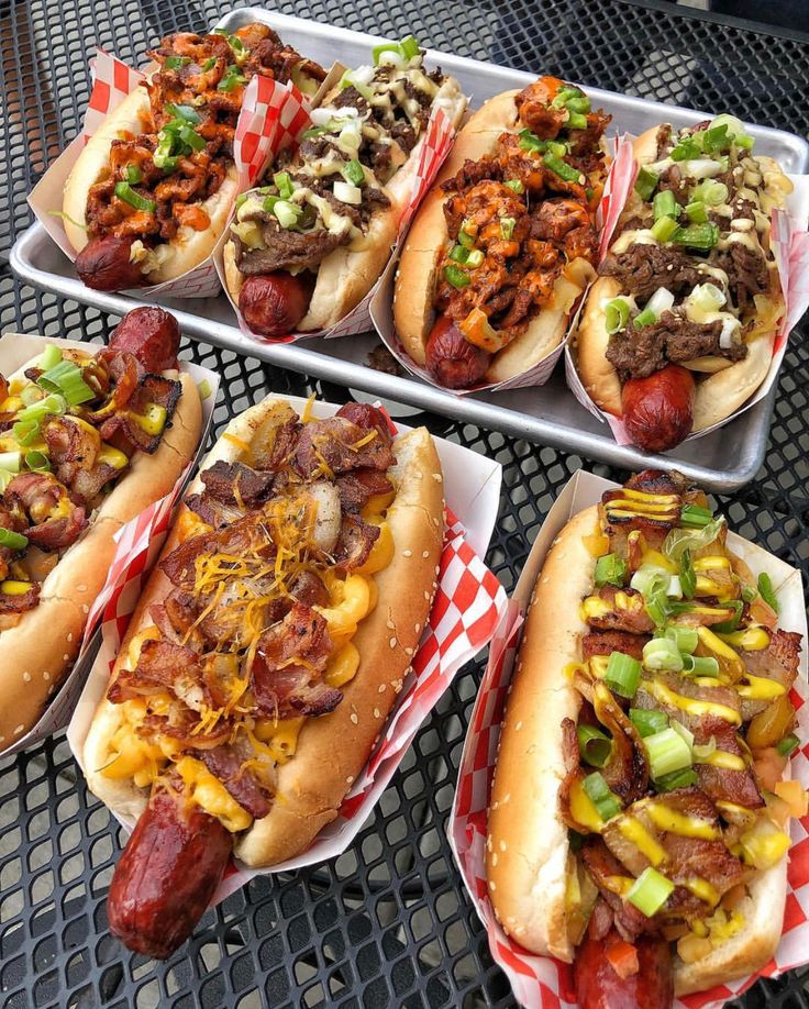 four trays filled with hot dogs covered in toppings