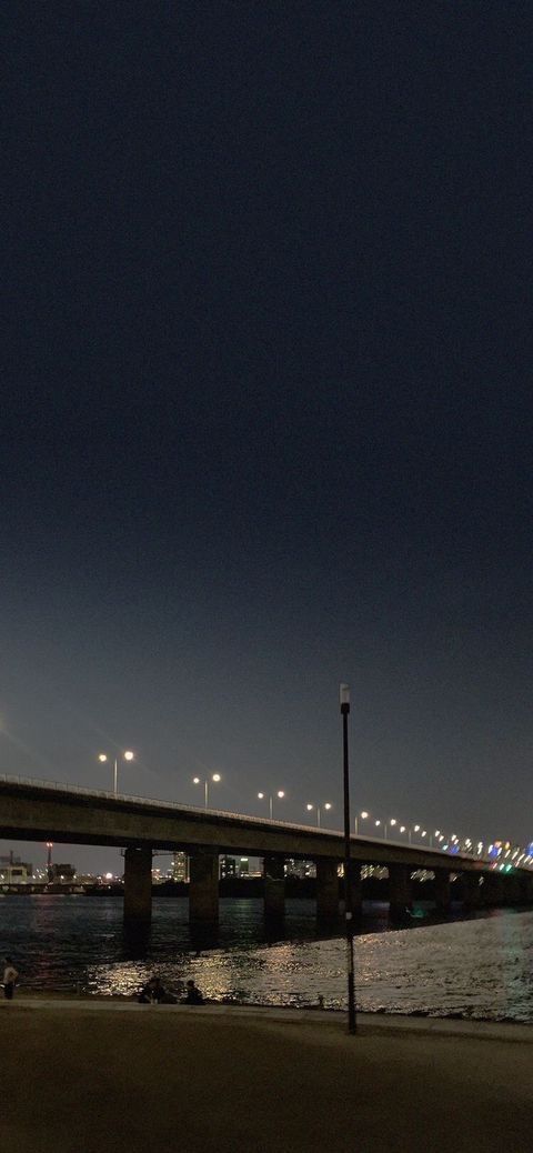 a bridge over water at night with lights in the sky and street lamps on either side