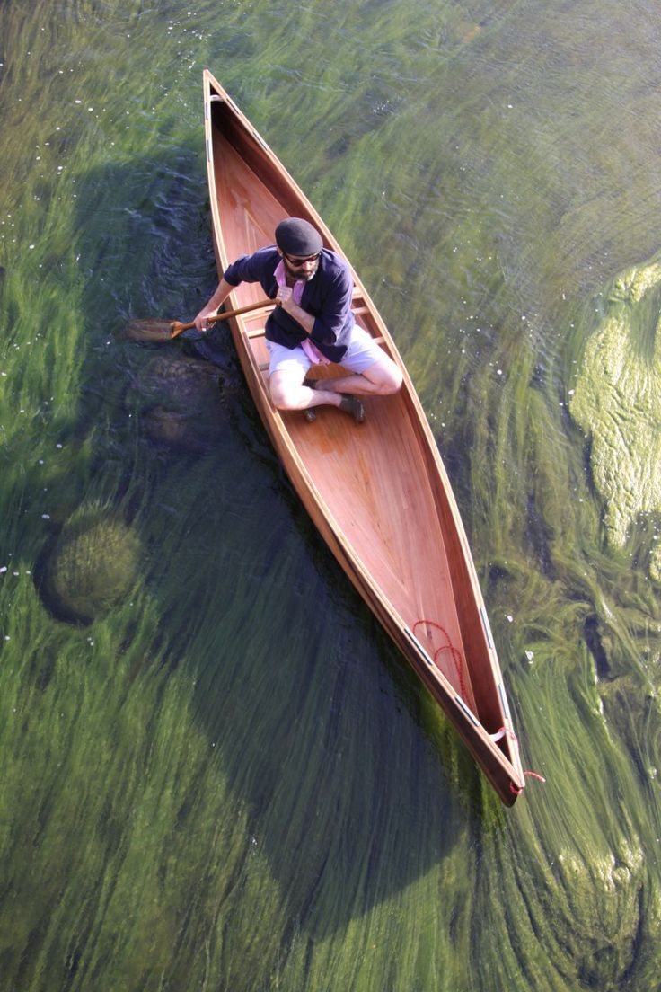 a man in a canoe paddling on the water with green algae growing around him