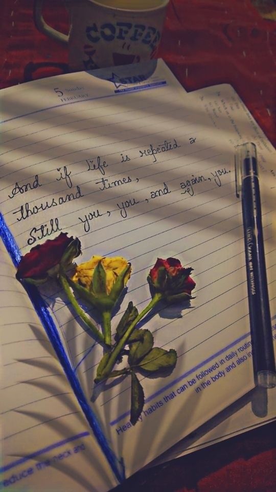 a notepad with roses and a pen on it next to a cup of coffee